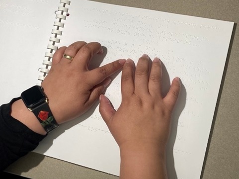 A person using a braille ballot; she is wearing a wedding ring and a watch with a rose on the band